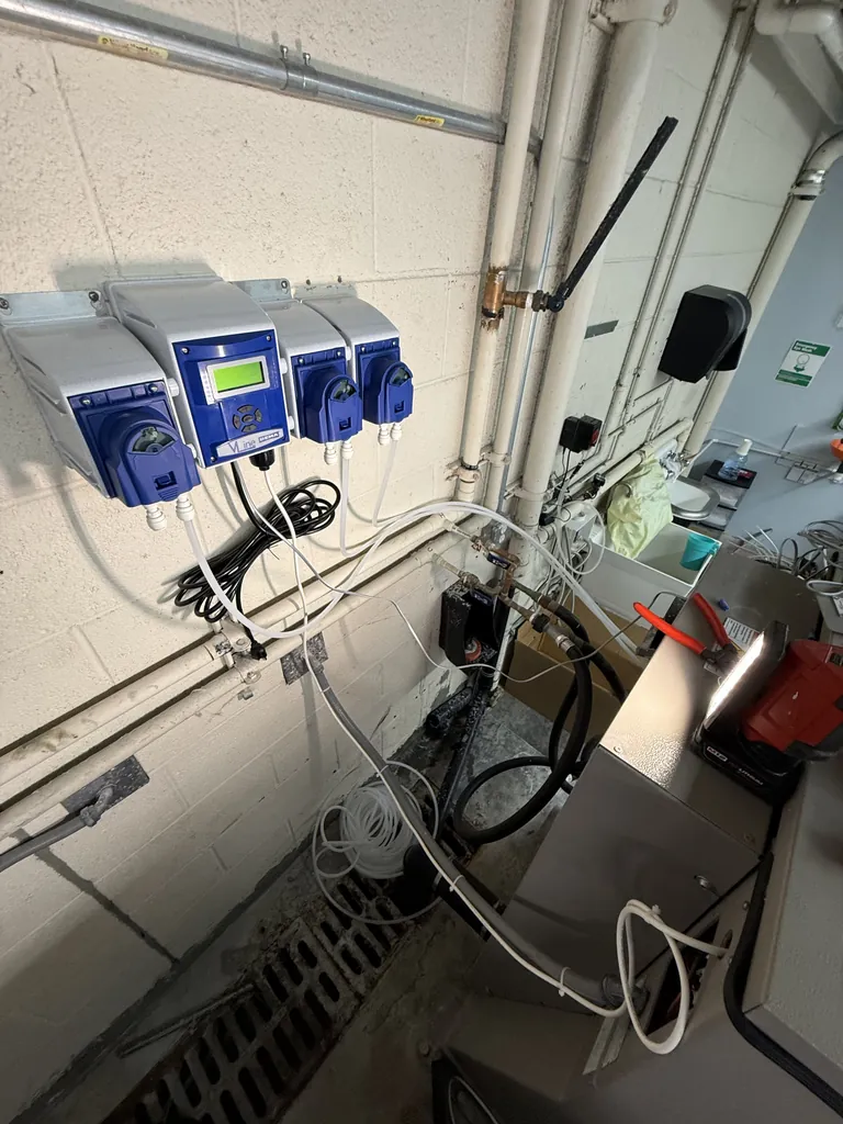 Wall-mounted multi-pump chemical dispensers with detergent, softener and bleach lines feeding a commercial washer