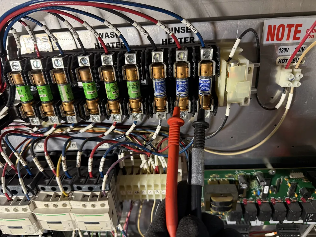 Testing the rinse heater fuses in a Douglas commercial dishwasher electrical panel with a multimeter