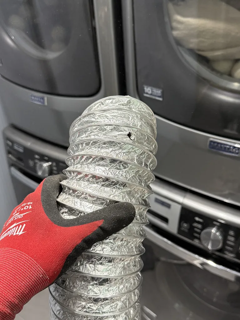 Technician holding new aluminum dryer vent duct during a stacked dryer repair in Henderson