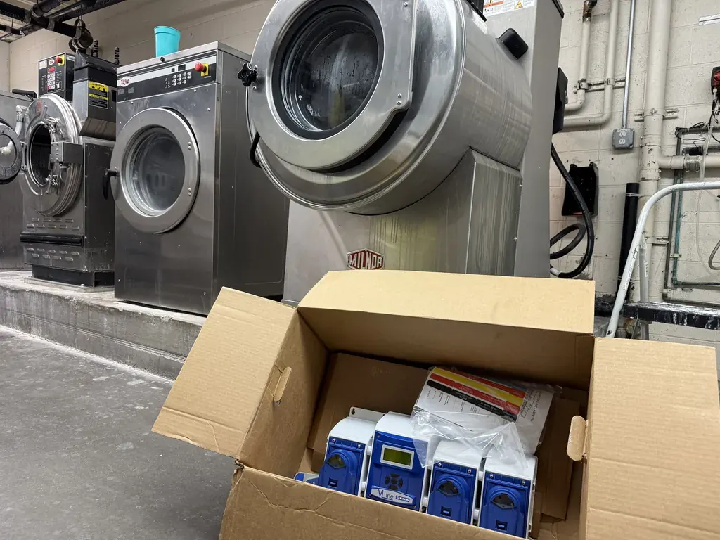 New automatic chemical dispenser pumps in front of commercial washer-extractors at a Summerlin senior living laundry